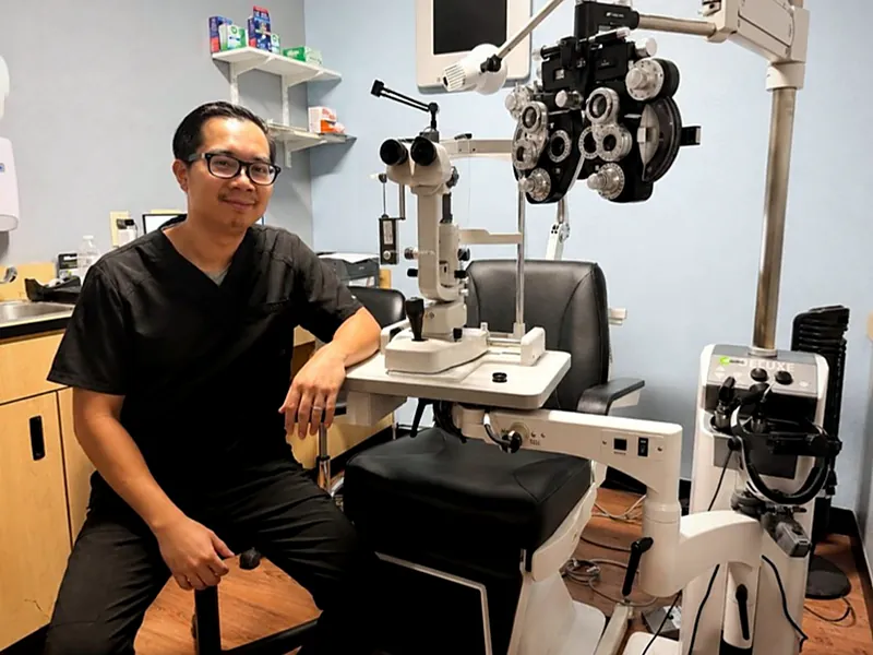 Dr. Ryan Nguyen seated beside the slit lamp and phoropter in the exam room