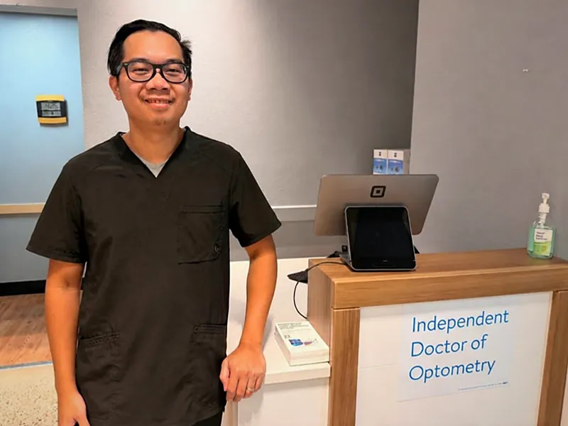 Dr. Ryan Nguyen at the front desk next to a sign reading Independent Doctor of Optometry